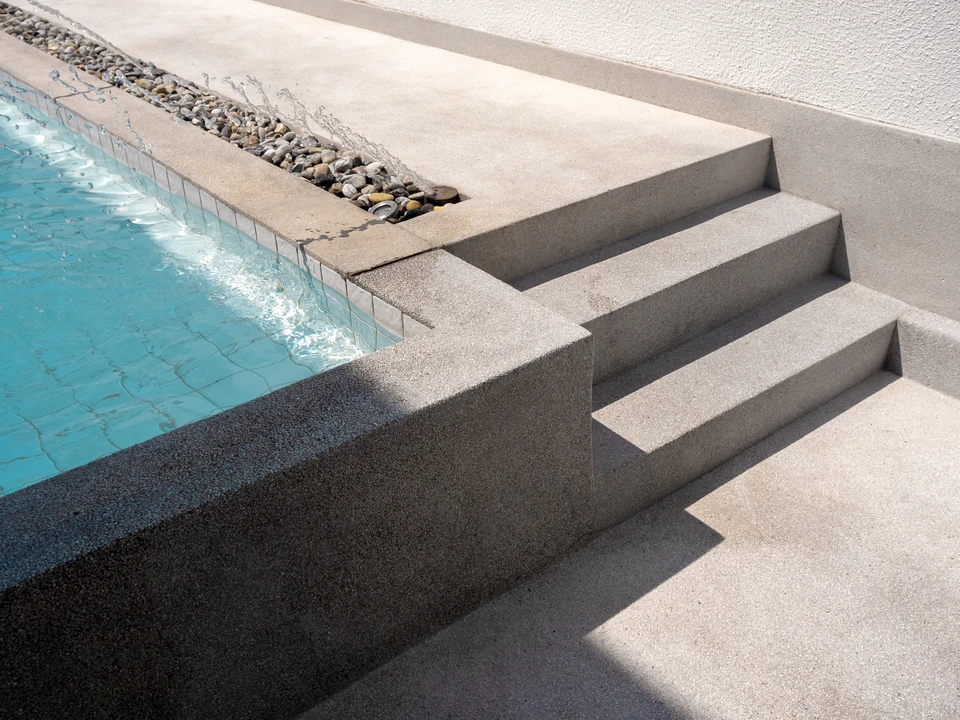 Aménagement extérieur de piscine avec margelles en béton gris disposées autour du bassin carrelé de mosaïques turquoise